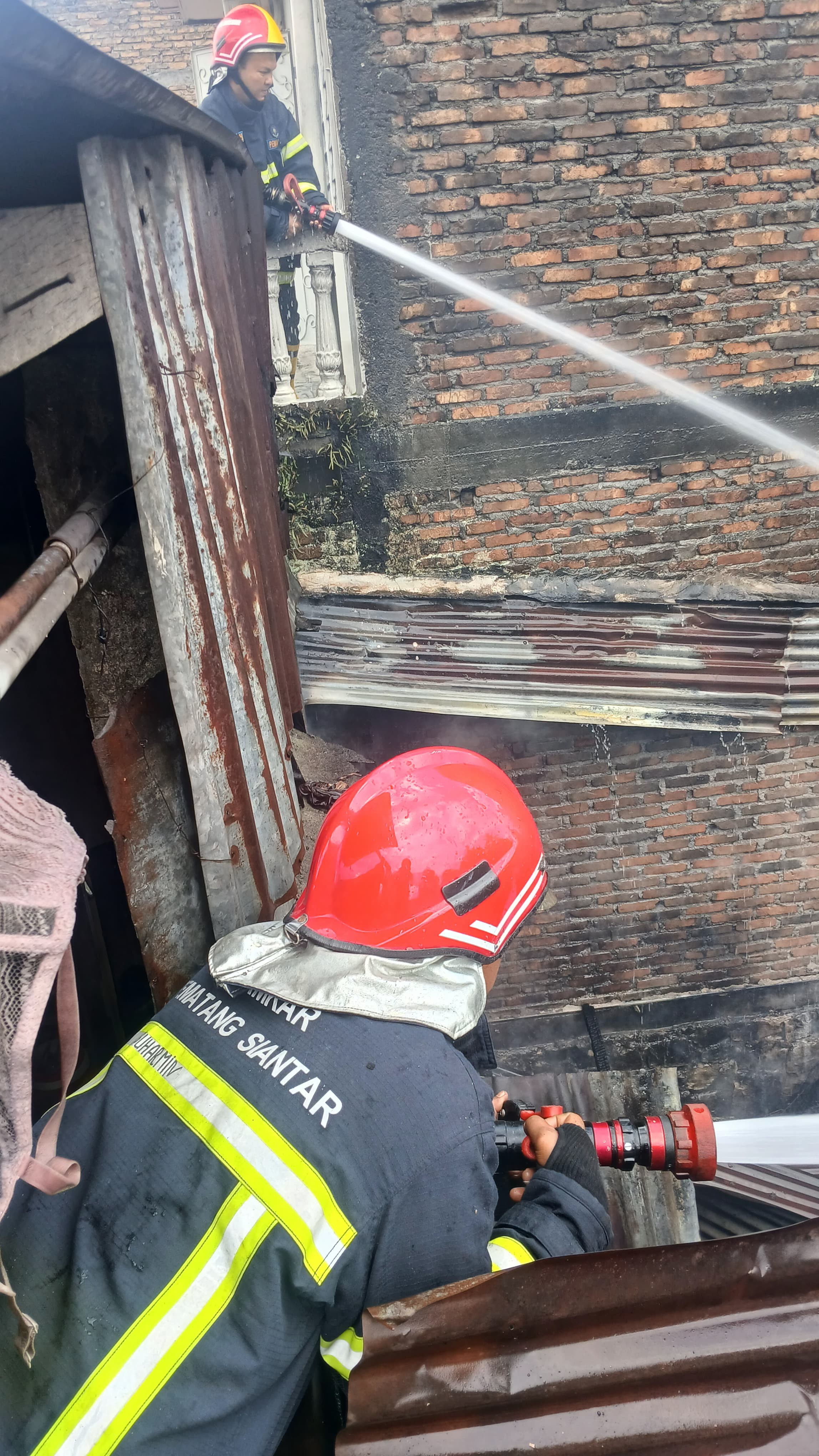 Personil Dinas Pemadam Kebakaran dan Penyelamatan melaksanakan pemadaman kebakaran rumah di Jl. Raku
